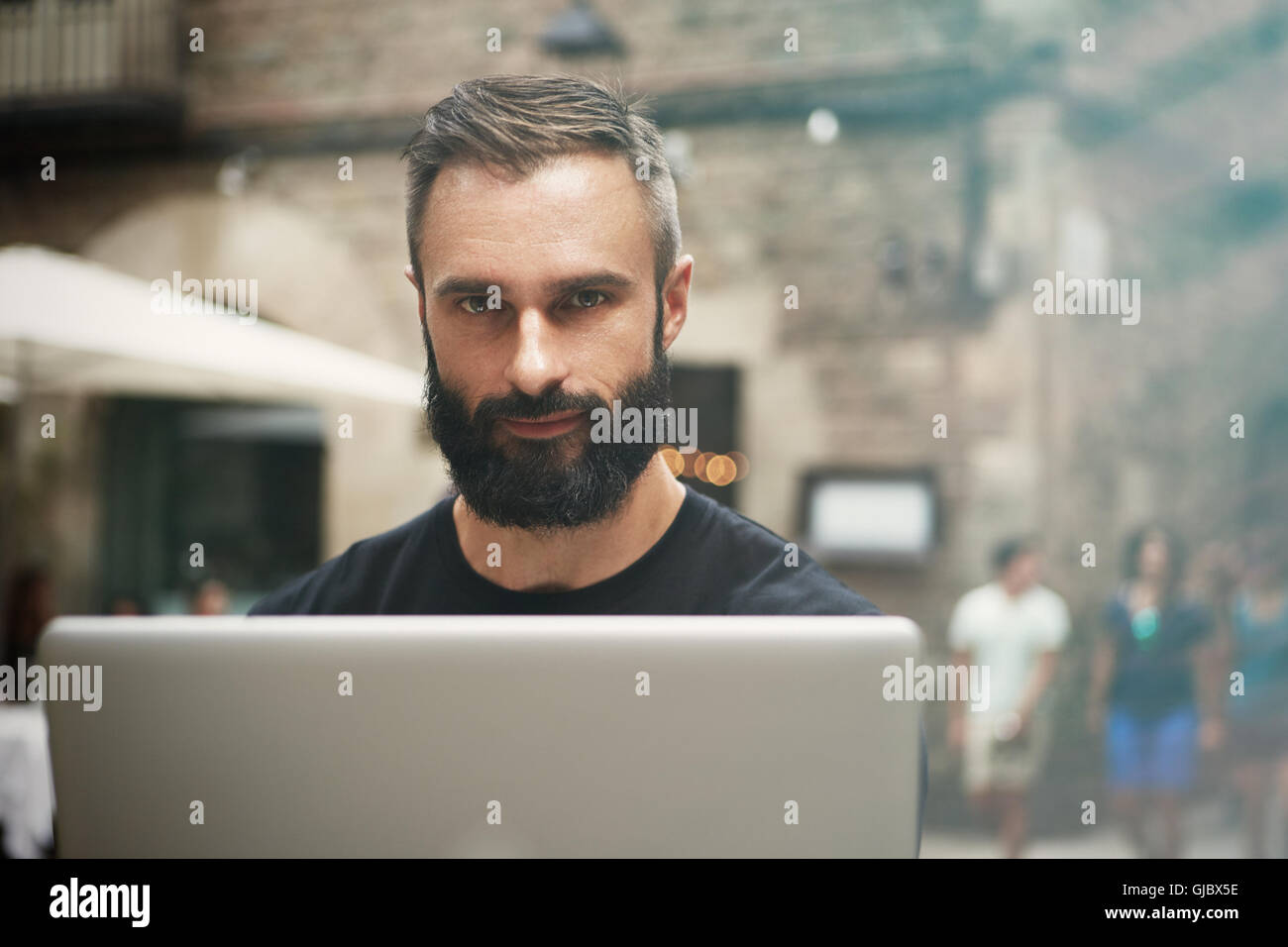 Closeup retrato guapo empresario barbudo vistiendo negro Tshirt Trabajo Urbano portátil Cafe.Joven Manager portátil de trabajo exterior.Coworking proceso Business Startup.fondo difuminado. Foto de stock
