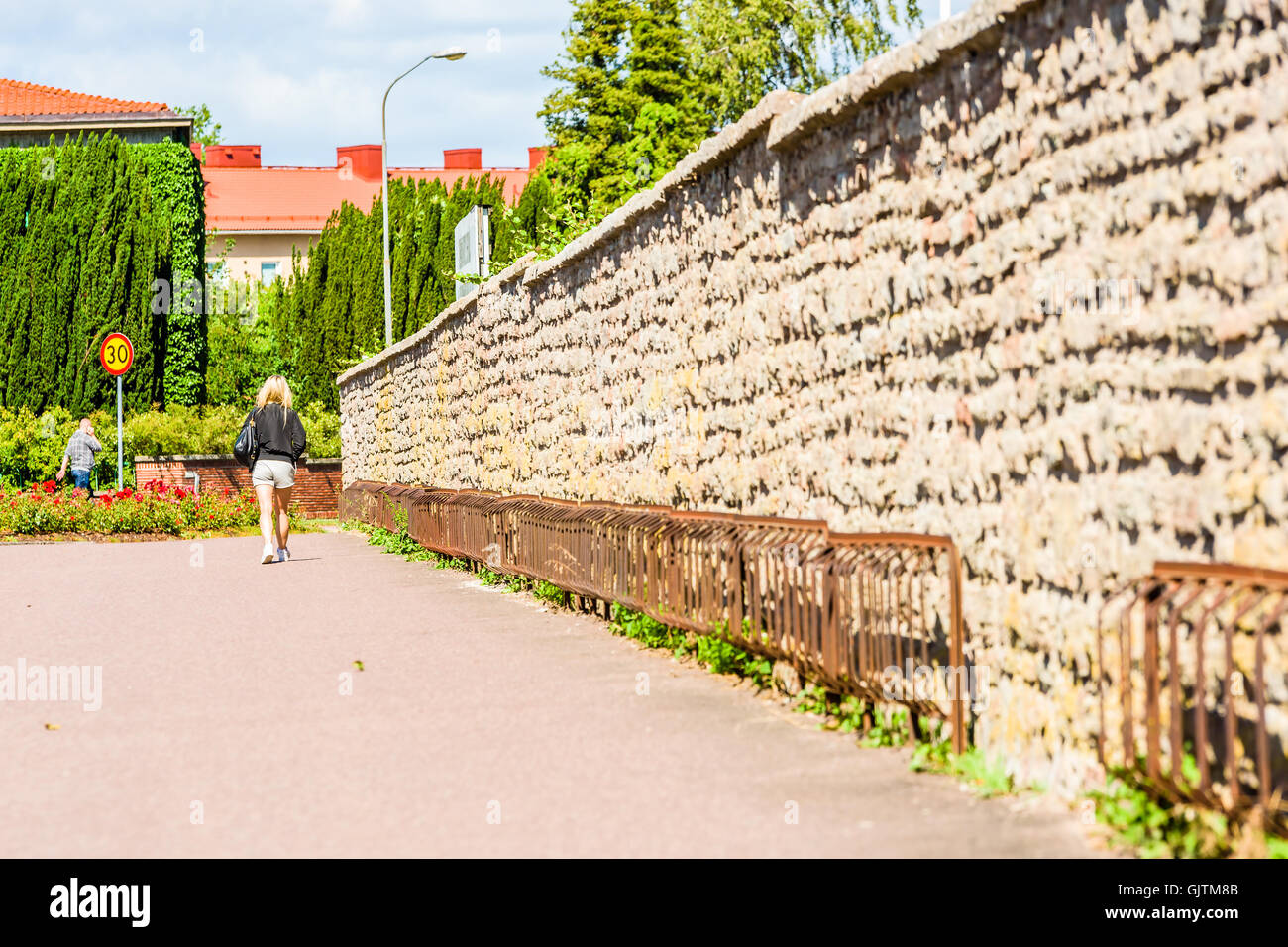 Kalmar, Suecia - Agosto 10, 2016: la mujer adulta joven camina lejos de usted a lo largo de una pared de piedra con bastidores de bicicletas vacías o soportes. Foto de stock