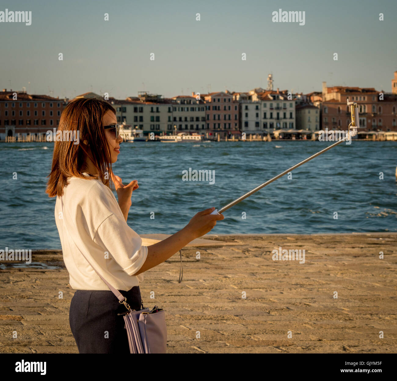 Hembra adulta joven asiático teniendo un selfie turística, utilizando un palo selfie; haciendo el signo V con los dedos. Venecia, Italia. Foto de stock