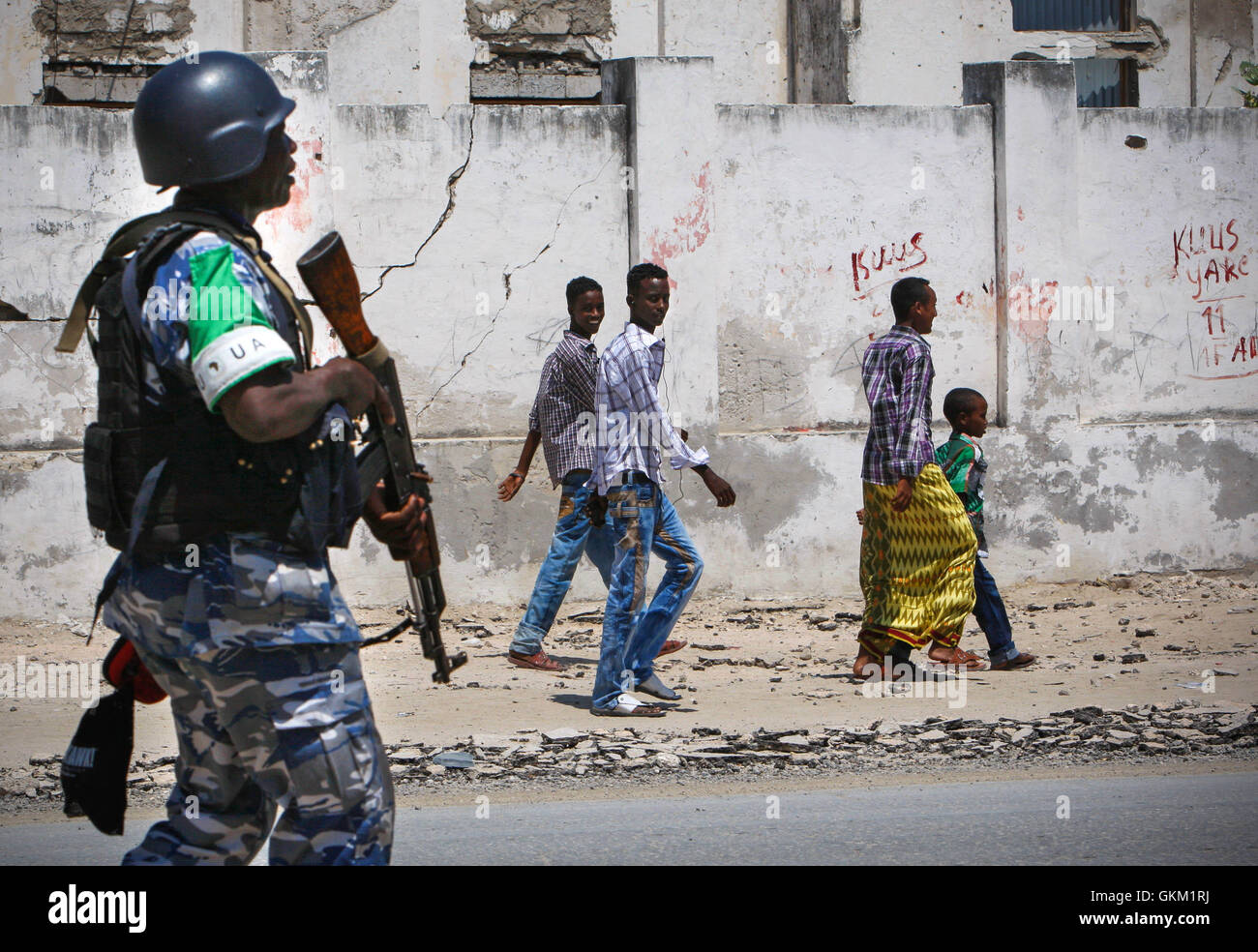 SOMALIA, MOGADISHU: En un panfleto foto tomada y liberado por el Grupo Africano Europea-estados unidas, Equipo de Apoyo a la información 09 de noviembre, jóvenes somalíes mirar mientras caminan más allá de un oficial de la policía de Uganda que sirve como parte de una unidad de policía constituida (FPU), con la misión de la unión de la Unión Africana en Somalia (AMISOM) camina pasado durante una patrulla a pie en la Kaa'ran el distrito en la capital somalí de Mogadishu. La AMISOM FPUs están colaborando con sus homólogos de la Policía Somalí (SPF) para ayudar a proporcionar seguridad en Mogadishu, además de la capacitación y asesoramiento de la SPF en técnicas policiales y prácticas. Foto de stock