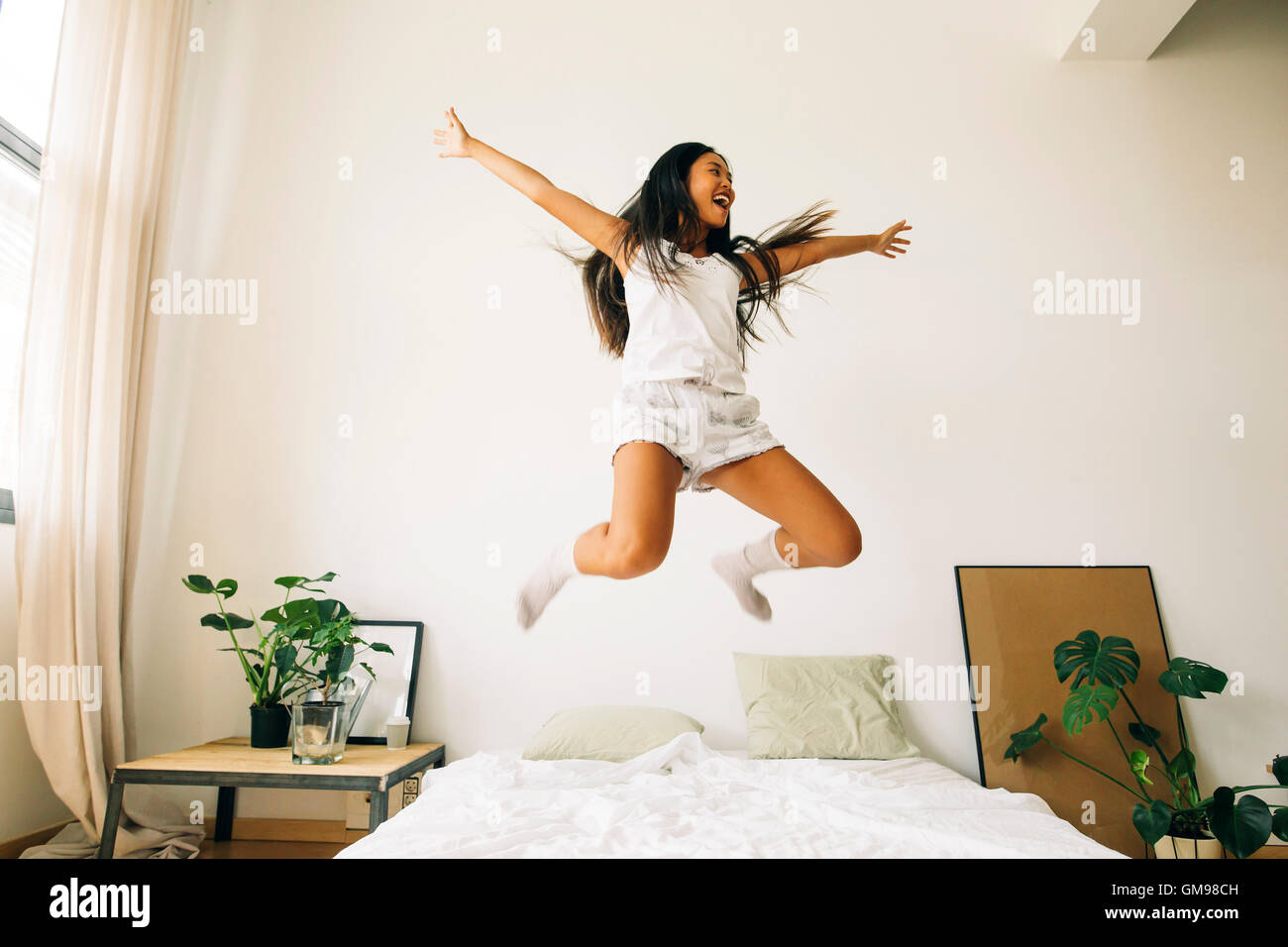 Exuberante mujer joven saltando sobre la cama Fotografía de stock - Alamy