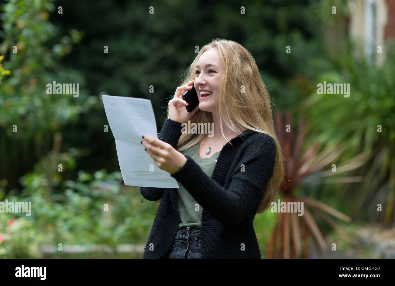 Un joven estudiante GCSE feliz en el teléfono después de recibir sus resultados de GCSE. Foto de stock