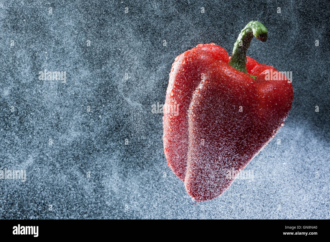 Pimiento rojo en un spray contra un fondo negro. Una serie de frutas y verduras en movimiento. Foto de stock