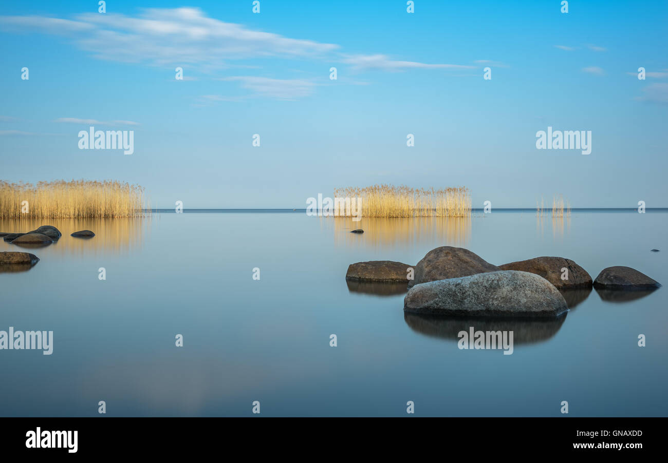 Grandes rocas y el azul del cielo se refleja en el lago Ladoga noche Foto de stock