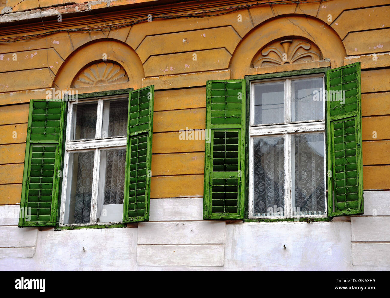 Abrir ventanas de madera con persianas verdes en la pared amarilla Foto de stock