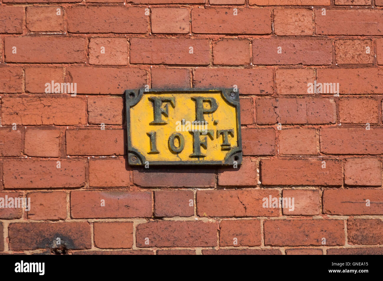 Un viejo cartel de hierro fundido F.P. 10 ft. sobre una pared de ladrillo rojo indicando un hidrante diez pies de la pared pie. Foto de stock