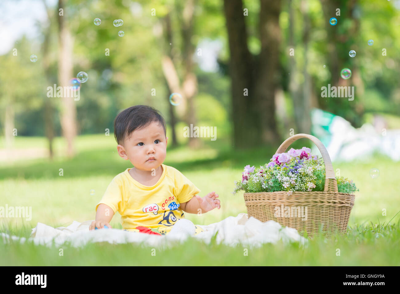 Asia Baby Boy sentado en el pasto verde en el parque con pompas de jabón Foto de stock