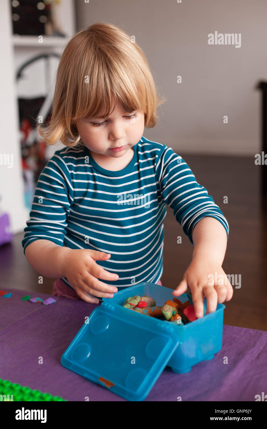 Rubio niño de dos años con rayas en blanco y azul jersey dentro de casa  almacenar plastilina en caja de plástico azul en la ficha color púrpura  Fotografía de stock - Alamy