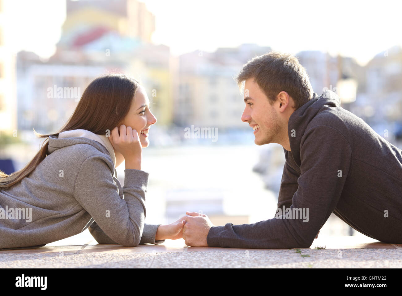 Vista lateral de una pareja de adolescentes dating y el coqueteo enamoramiento buscando mutuamente tumbado en el suelo en un puerto Foto de stock