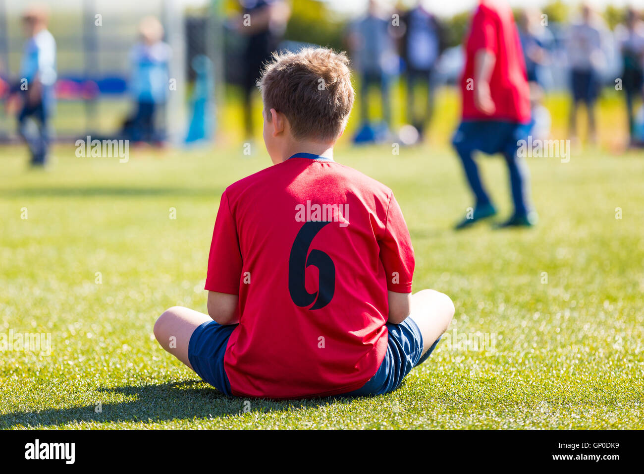 Niño vestido en ropa deportiva sentado en el pasto verde del estadio  deportivo. Los niños está esperando su turno para jugar fútbol footbal mat  Fotografía de stock - Alamy