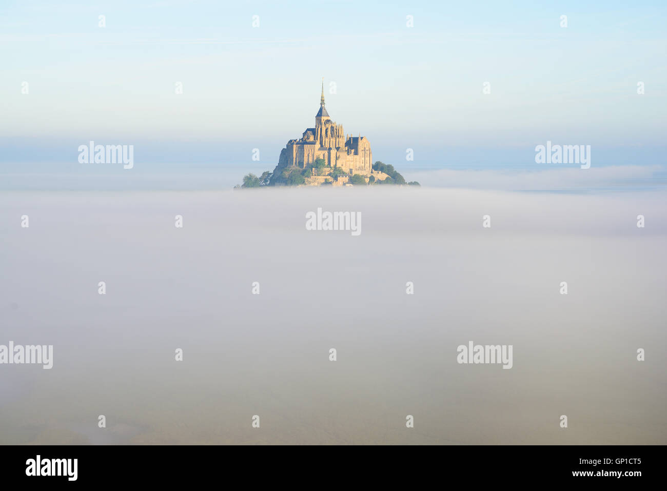 VISTA AÉREA. Abadía en un pico aislado sobre la niebla temprana de la mañana. Mont Saint-Michel, La Mancha, Normandía, Francia. Foto de stock