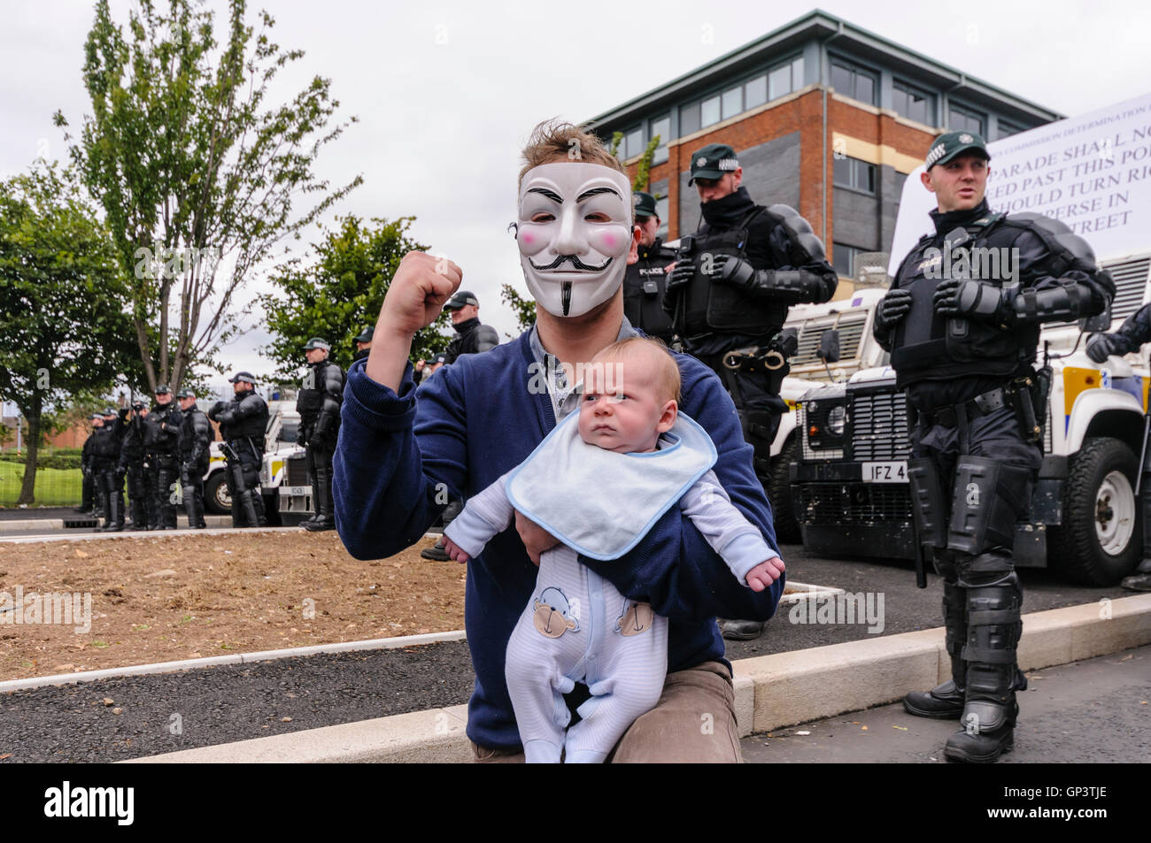 Un hombre vestido con un 'anónimo' Guy Fawkes mask y sosteniendo un bebé, ofrece una desafiante salute delante de una fila de PSNI policías Fotografía de stock - Alamy