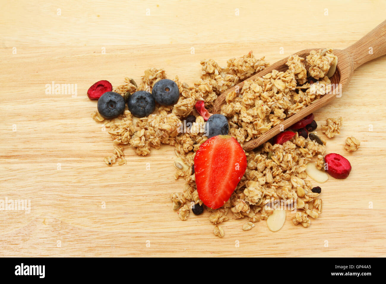 Granola y fruta fresca con una cuchara de madera sobre una tabla de cortar Foto de stock
