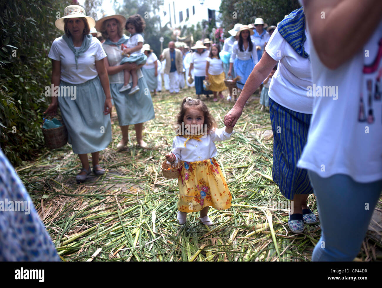 Una mujer llevando de la mano de su hija, vestida como una cosechadora caminar en una calle cubierta por juncia durante el Corpus Christi Foto de stock