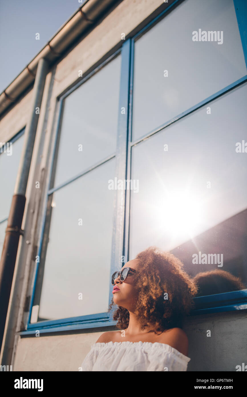 Foto de un bonito joven mujer africana sentados al aire libre y mirando a otro lado. Mujer con gafas de sol sentado afuera. Foto de stock