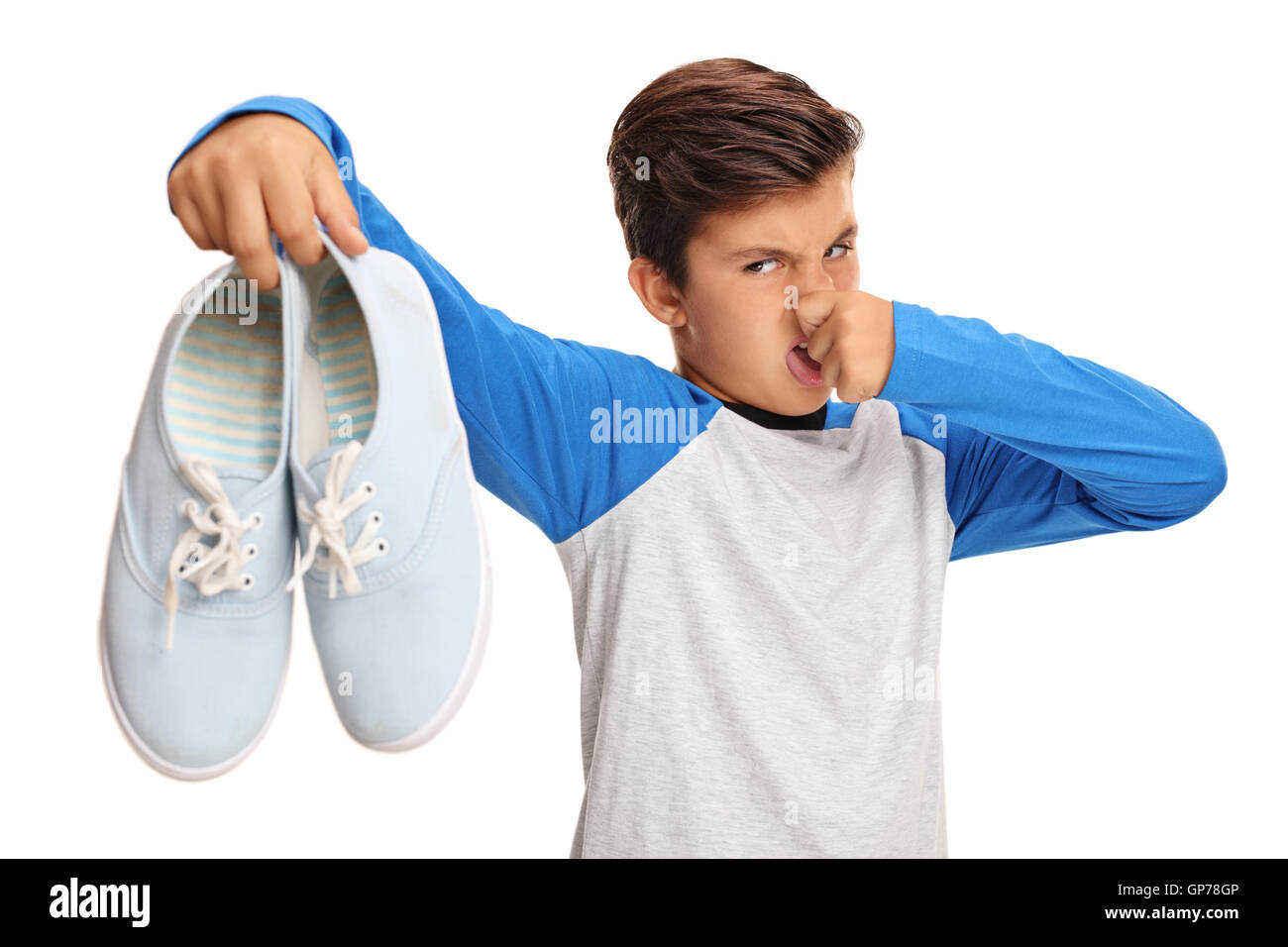 Disgustado niño sosteniendo un par de zapatos malolientes aislado sobre fondo blanco. Foto de stock