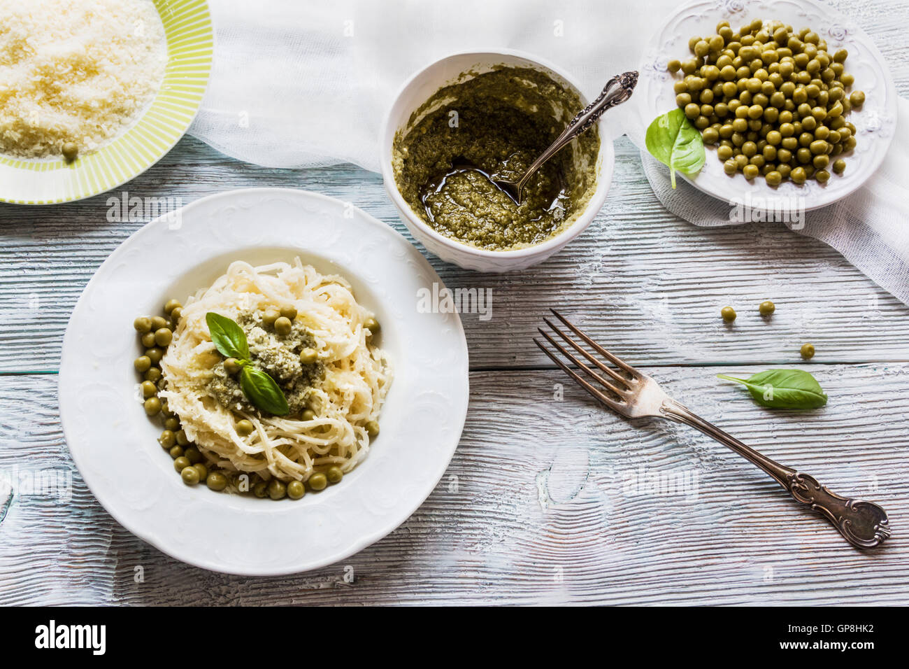 Espaguetis con salsa pesto sobre blanco vintage placa, queso rallado, hojas de albahaca fresca y judias verdes sobre fondo de madera Foto de stock