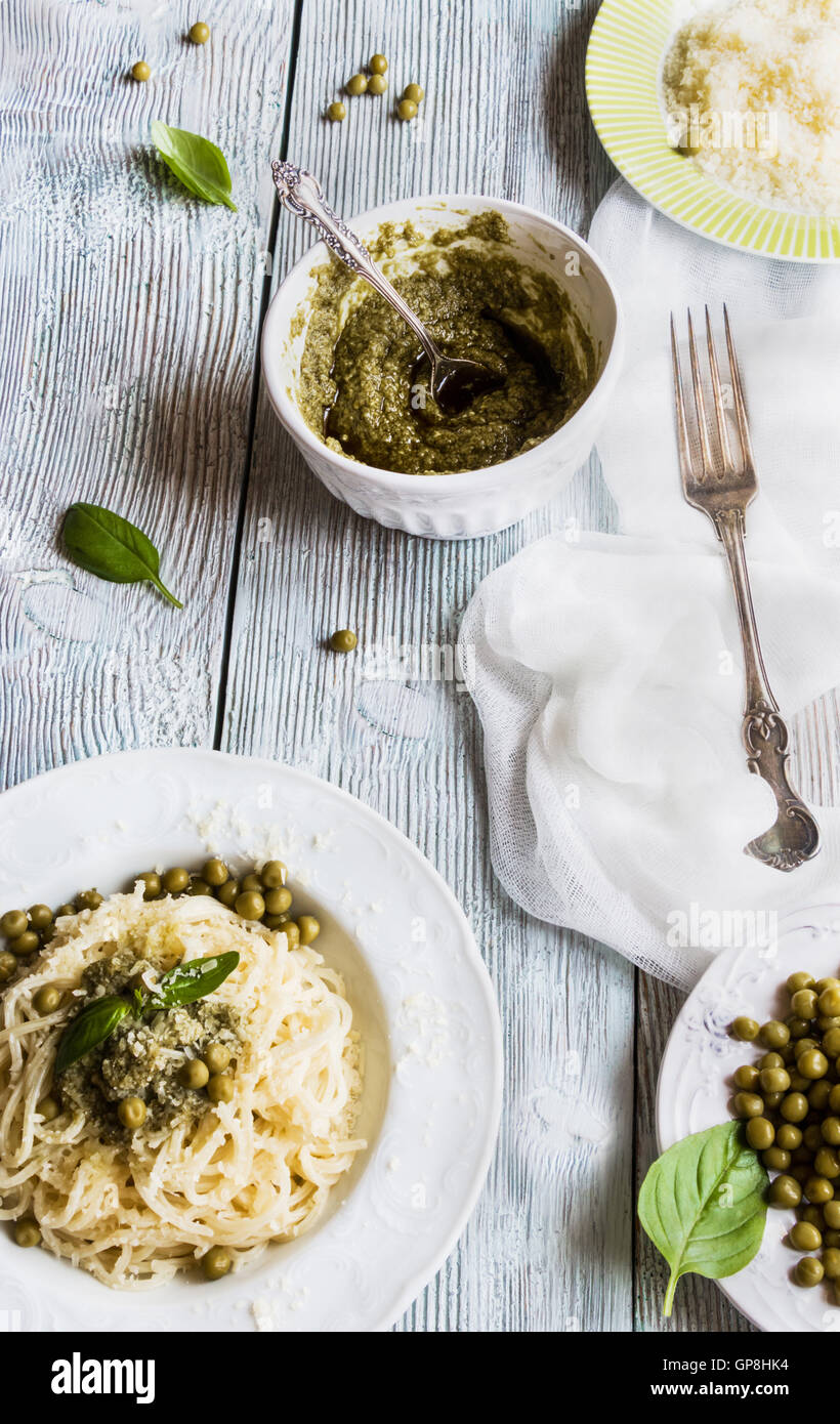 Espaguetis con salsa pesto sobre blanco vintage placa, queso rallado, hojas de albahaca fresca y judias verdes sobre fondo de madera Foto de stock