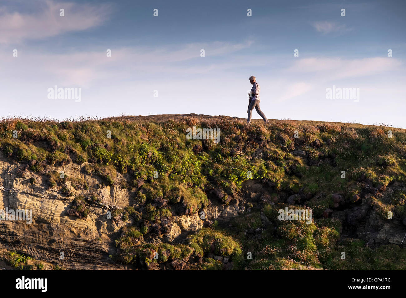 Una mujer pasea en la costa de Porth isla en Newquay, Cornwall. Foto de stock