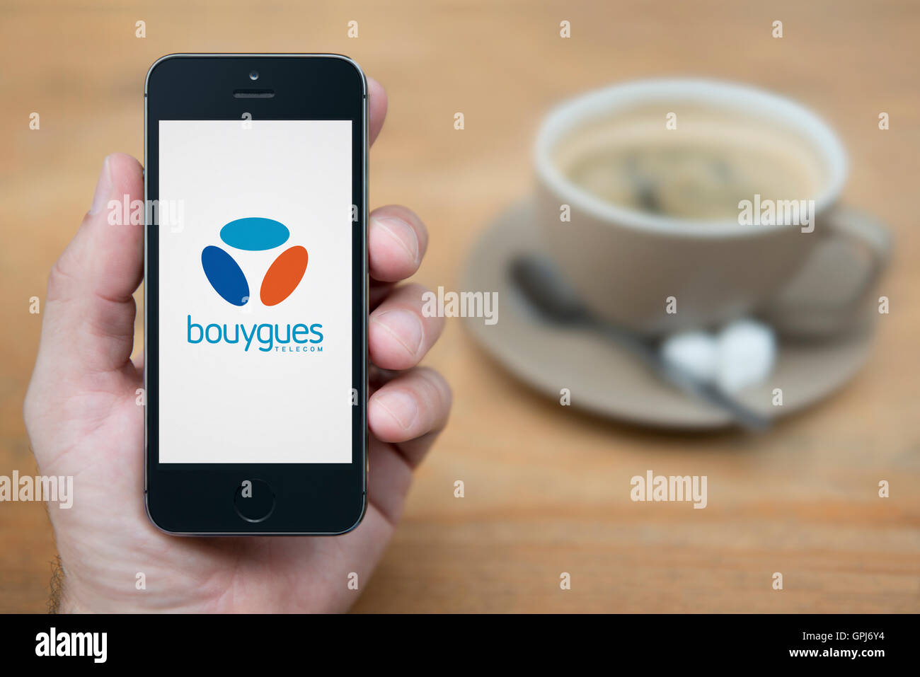 Un hombre mira su iPhone que muestra el logotipo del operador de telecomunicaciones Bouygues Telecom, con café (uso Editorial solamente). Foto de stock