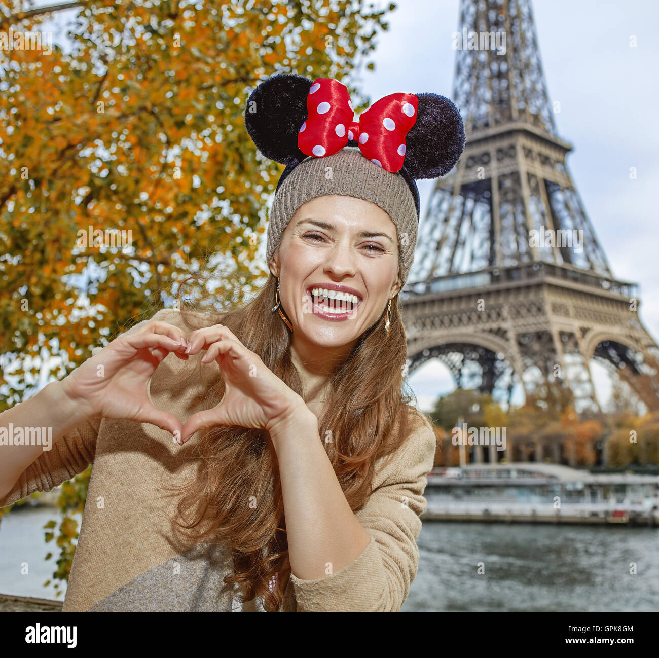 Vacaciones de otoño perfecto en Disneyland y en París. Retrato de turista  contento mujer vistiendo Minnie Mouse orejas en terraplén en París,  Francia, mostrando las manos en forma de corazón Fotografía de