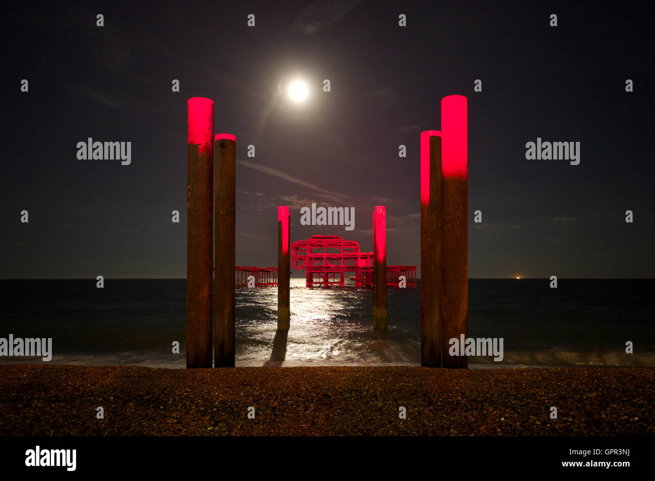 Brighton Beach, West Pier y el mar iluminado por la luz de la luna con un rayo rojo de luz proyectada sobre el muelle Foto de stock