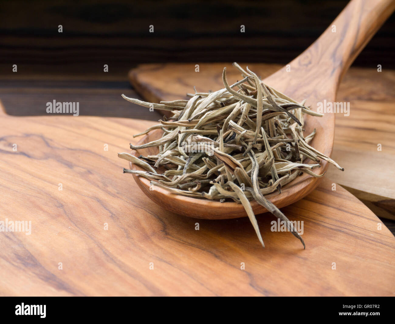 Puntas de plata té blanco en la cuchara de madera de olivo en el tablero de madera de olivo Foto de stock