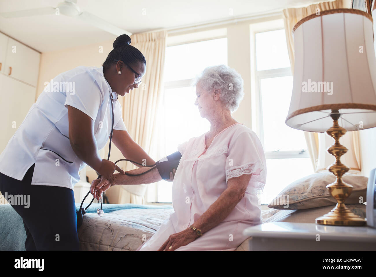Enfermera haciendo la medición de la presión sanguínea de un paciente mujer de más edad. Doctor el chequeo de la presión arterial de una anciana en o Foto de stock