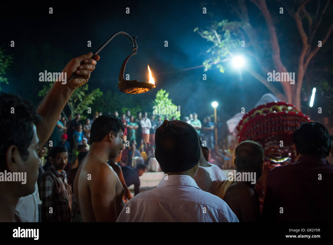 Un hombre sostiene una llama aloft para iluminar las actuaciones en una theyyam ritual en una aldea cerca de Keralan norte Kannur Foto de stock