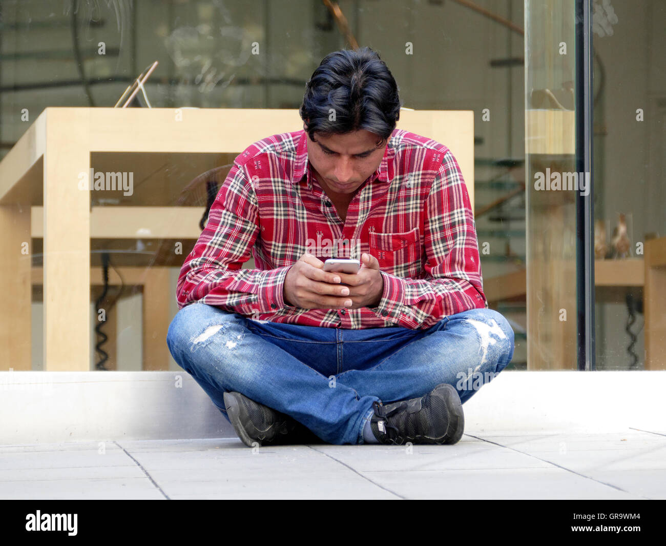 El hombre o la pareja conectar el smartphone a un punto fuera de una tienda de Apple. Foto de stock
