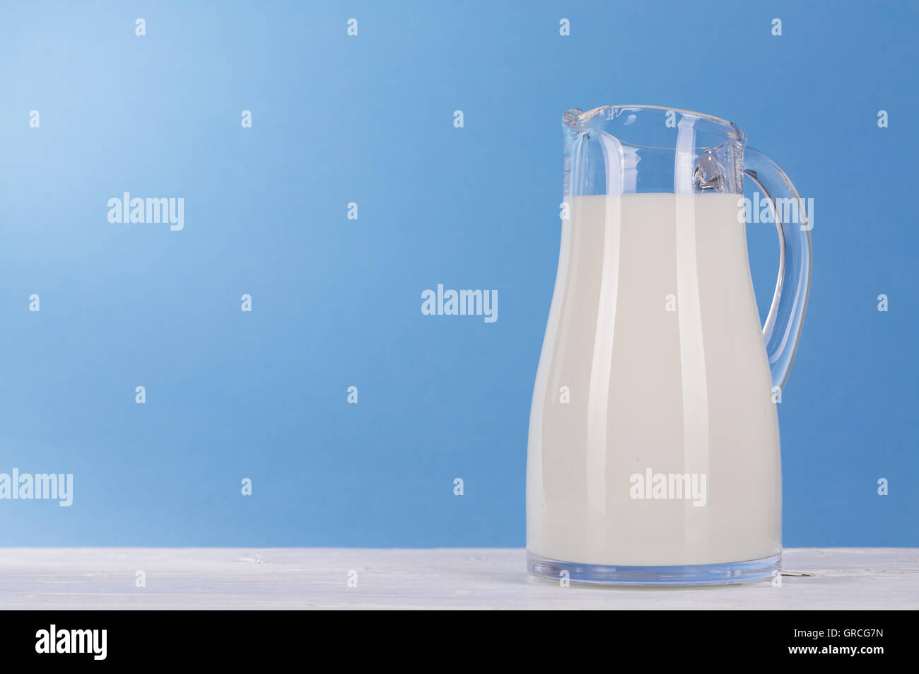 Jarra de leche sobre la plancha de madera blanca y luz de fondo azul Foto de stock