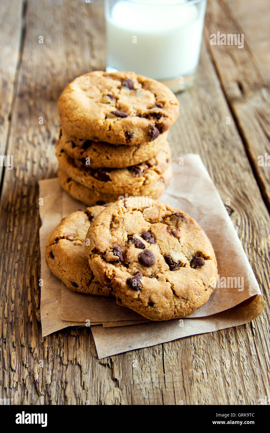 Las galletas con trocitos de chocolate con leche sobre papel y tabla de madera rústica Foto de stock