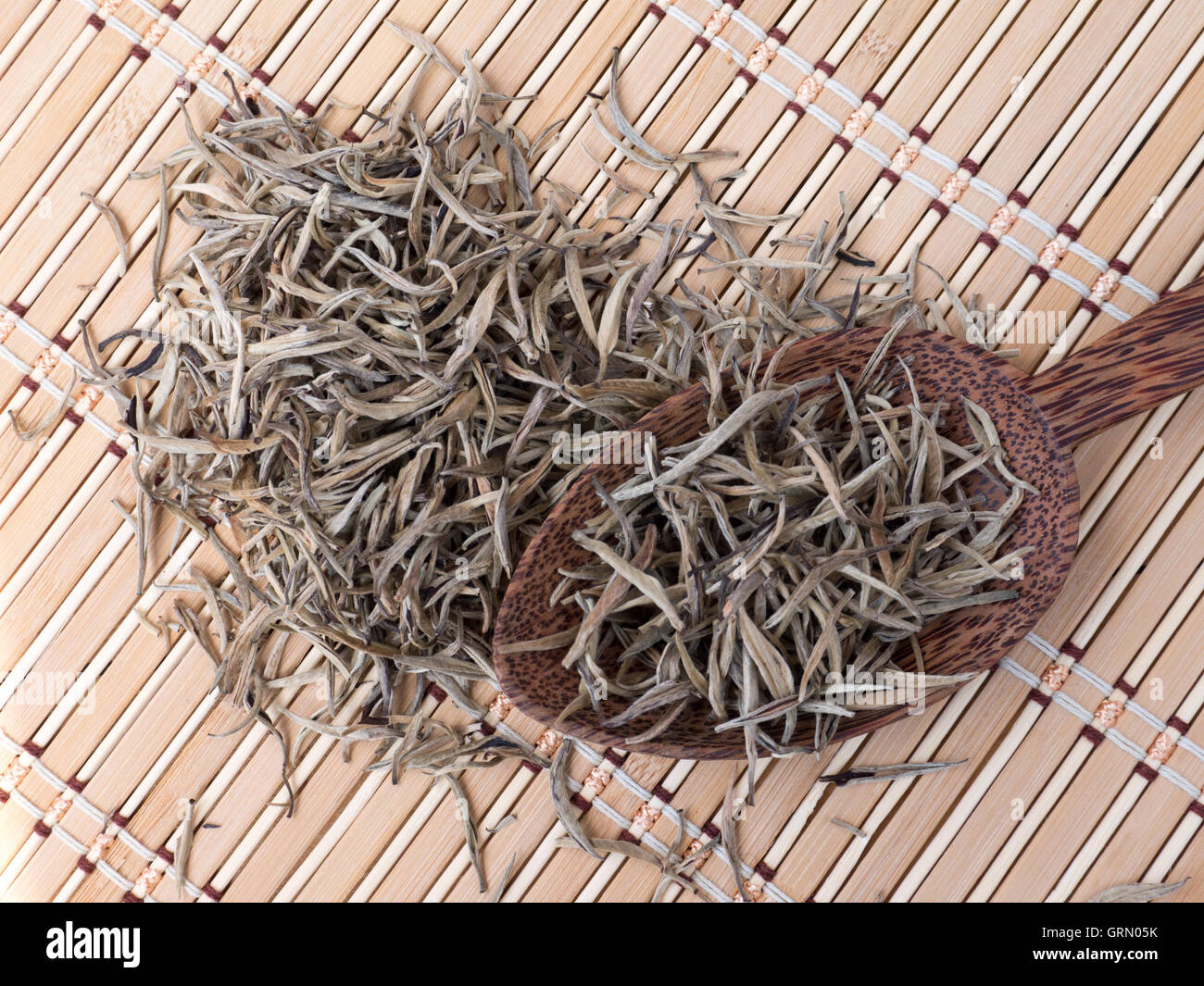 Puntas de plata de té blanco coco en la cuchara de madera sobre el bambú mat Foto de stock