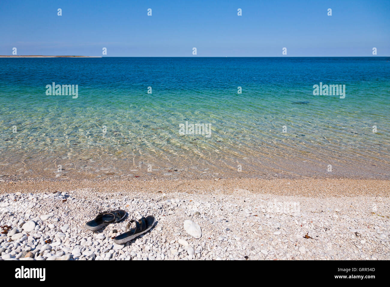 Par de sandalias en una playa de cantos rodados de piedra Foto de stock