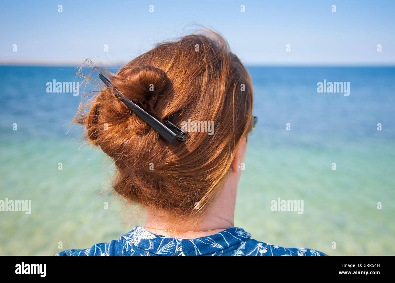 Mujer con pelo largo y vistiendo su pelo en un nudo contemplando el mar Foto de stock