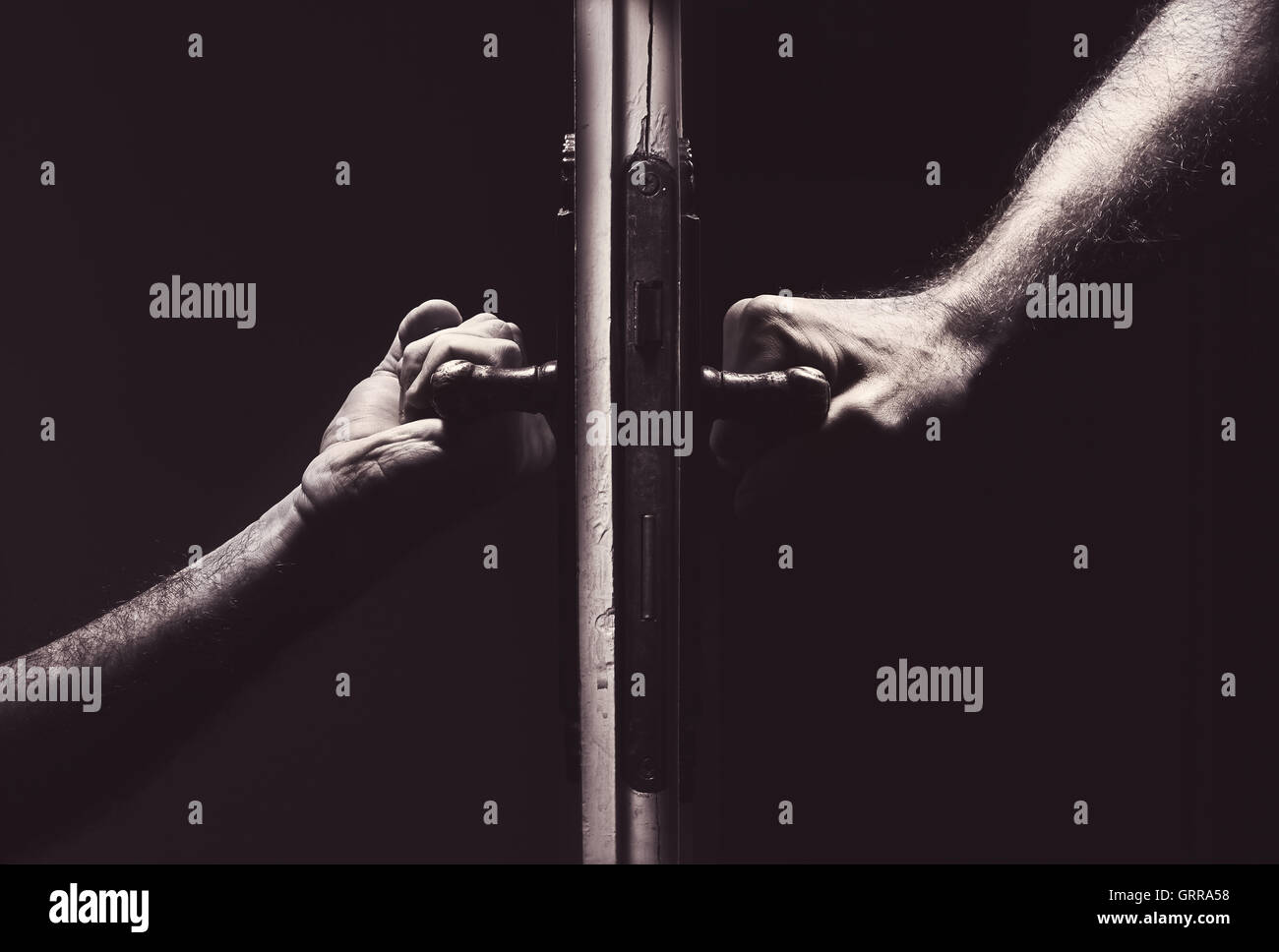 Composición conceptual acerca de malas relaciones, manos masculinas en distintos lados de una puerta. Foto de stock