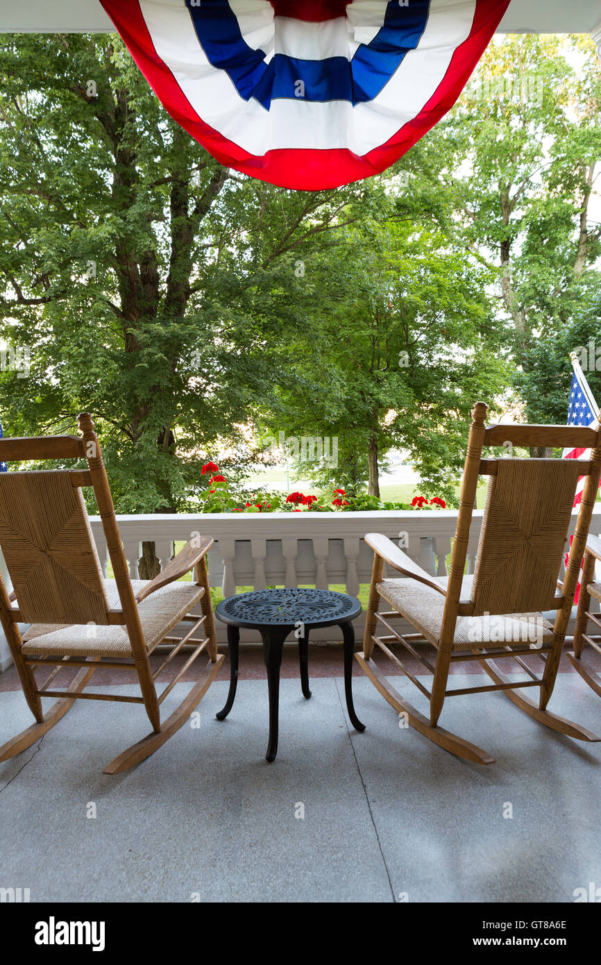 Dos mecedoras de madera con una pequeña mesa en la terraza con la bandera  americana conceptual al frente de altos árboles verdes en el jardín  Fotografía de stock - Alamy