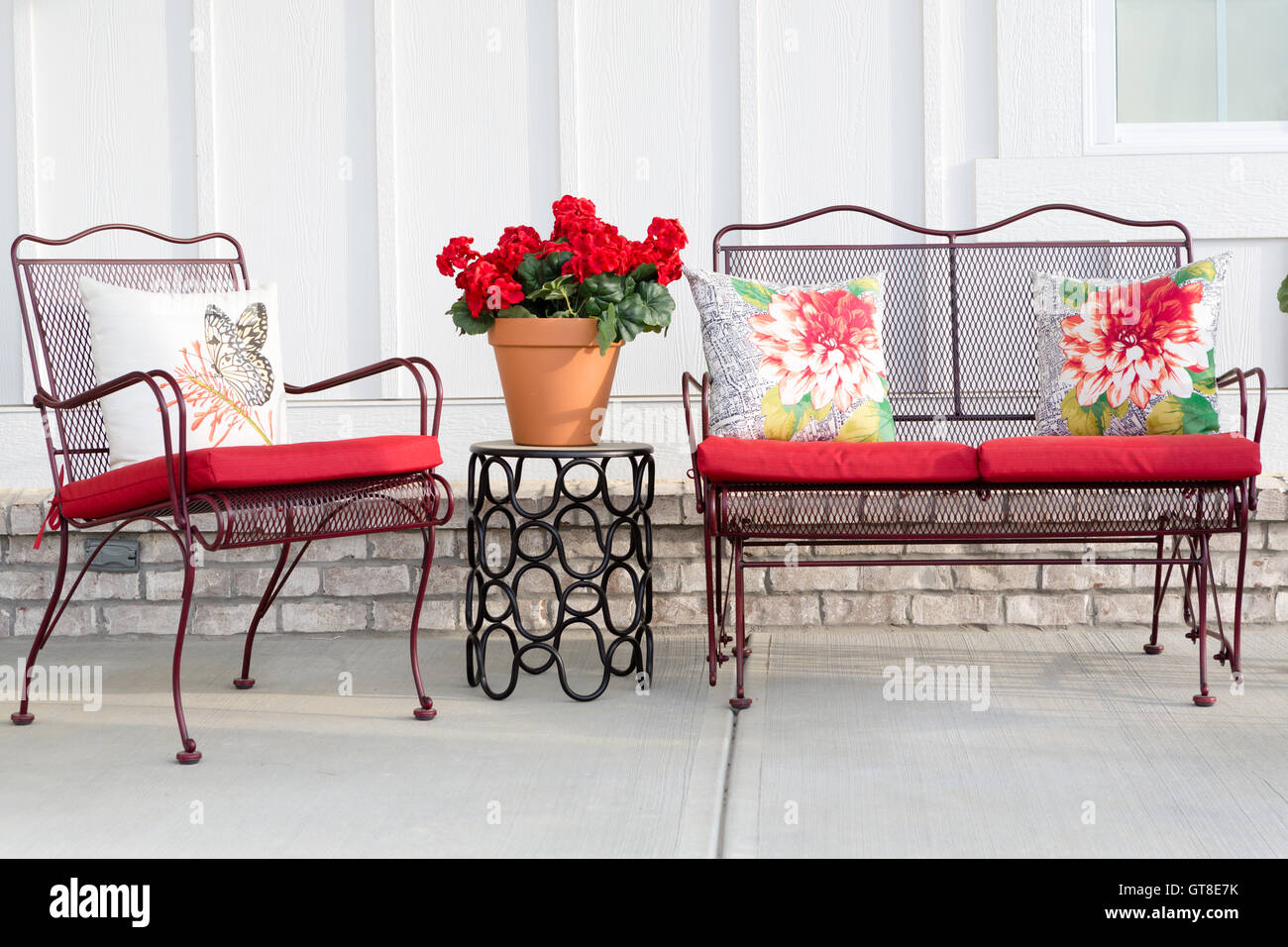 testigo Influencia Sumergir Coloridos muebles de jardín de hierro forjado con cojines rojos vibrantes y  un rojo macetas de geranios de pie sobre un patio delantero al aire libre o  Fotografía de stock - Alamy