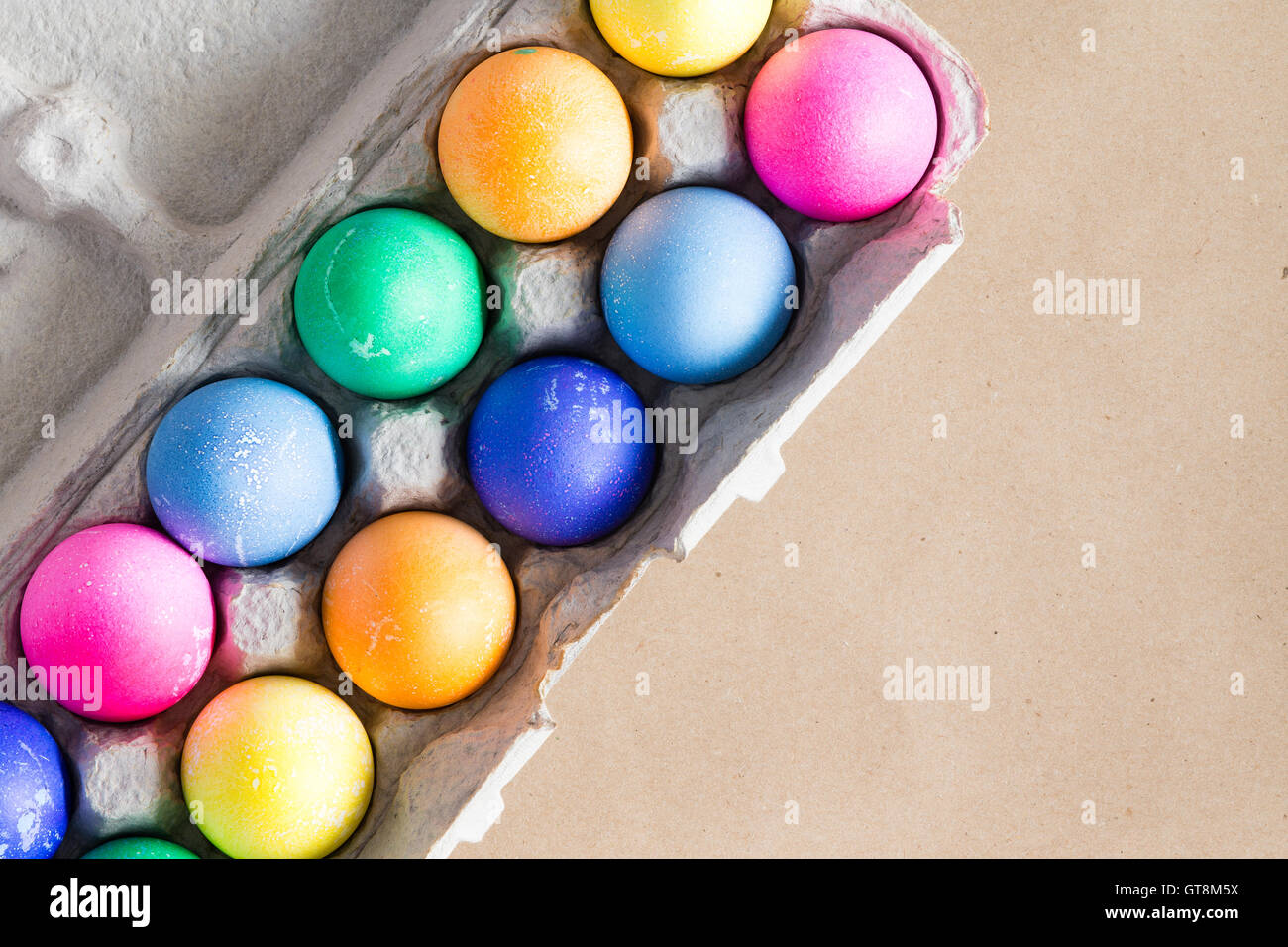Vibrante colorido teñidas a mano los huevos de Pascua en una caja de huevos de cartón visto desde arriba sobre un fondo de color beige con copia espacio para su g Foto de stock