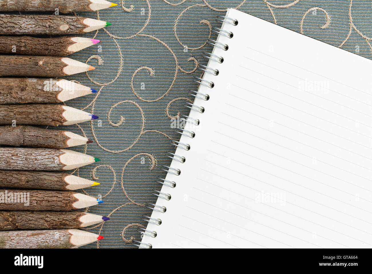Lápiz de color, crayones formando un borde lateral con un cuaderno de espiral en blanco con copia espacio y patrón de espiral en la tabla Foto de stock
