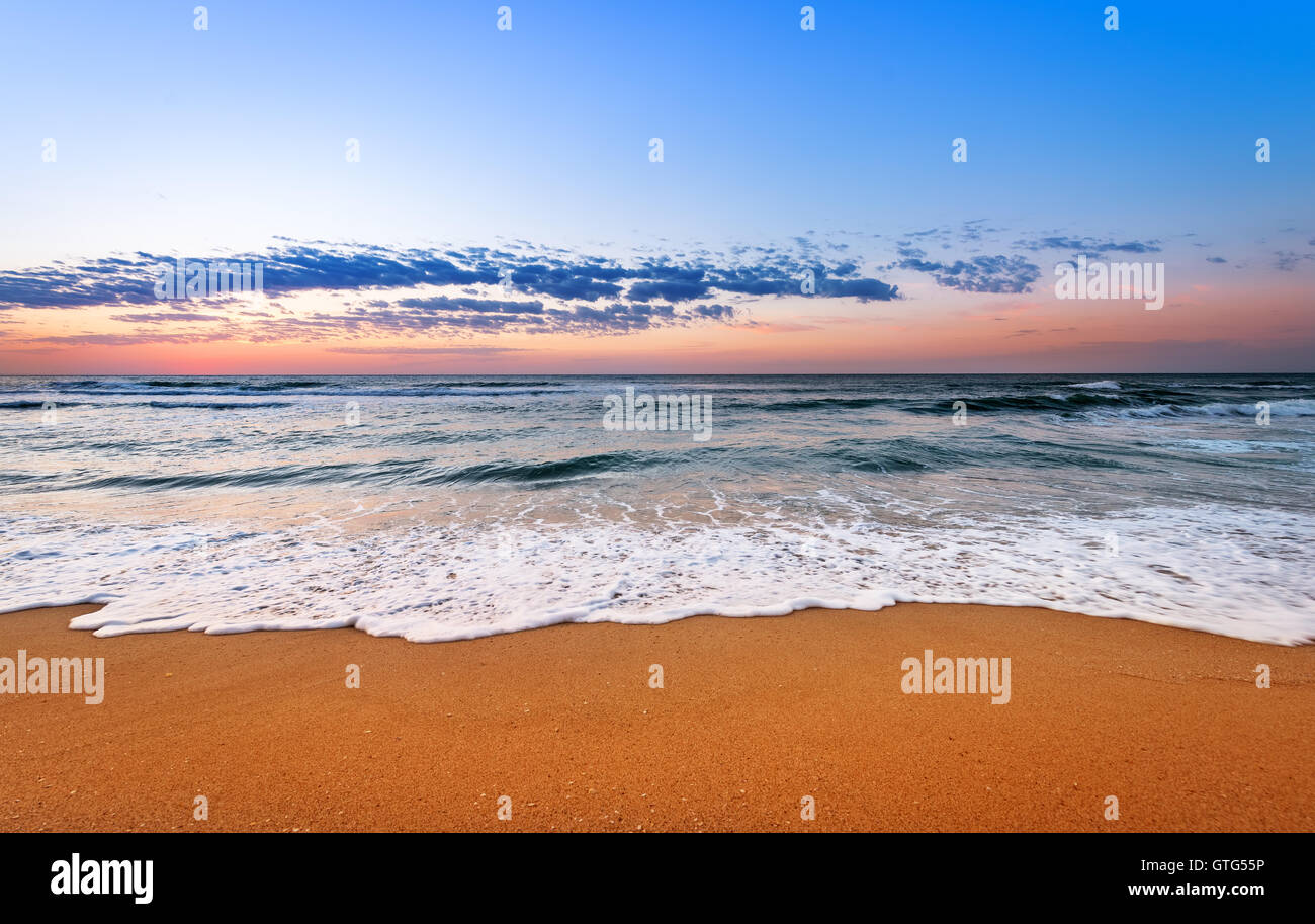 Colorido ocean beach amanecer con un cielo de azul profundo y rayos de sol. Foto de stock