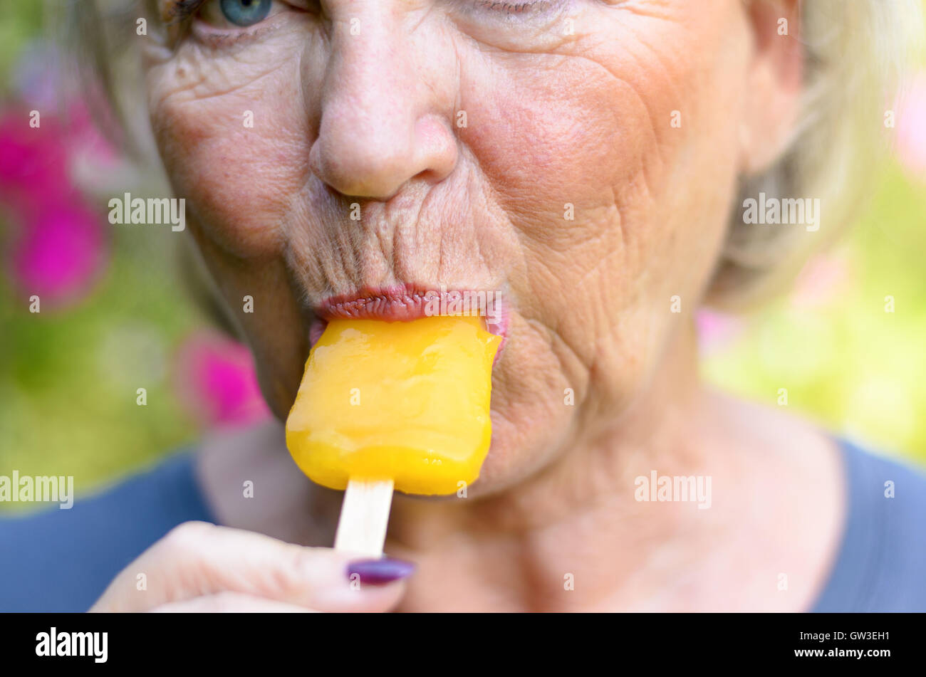 Mujer senior de chupar un helado de naranja lolly afuera en un día de  verano refrescarse del calor, Cerrar vista recortada en su mo Fotografía de  stock - Alamy