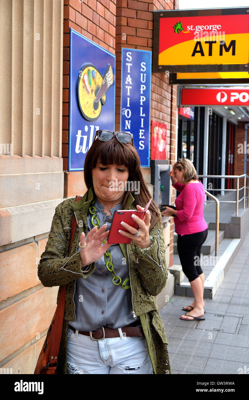 Las mujeres que usan teléfonos móviles y acceso a ATM Bank Foto de stock