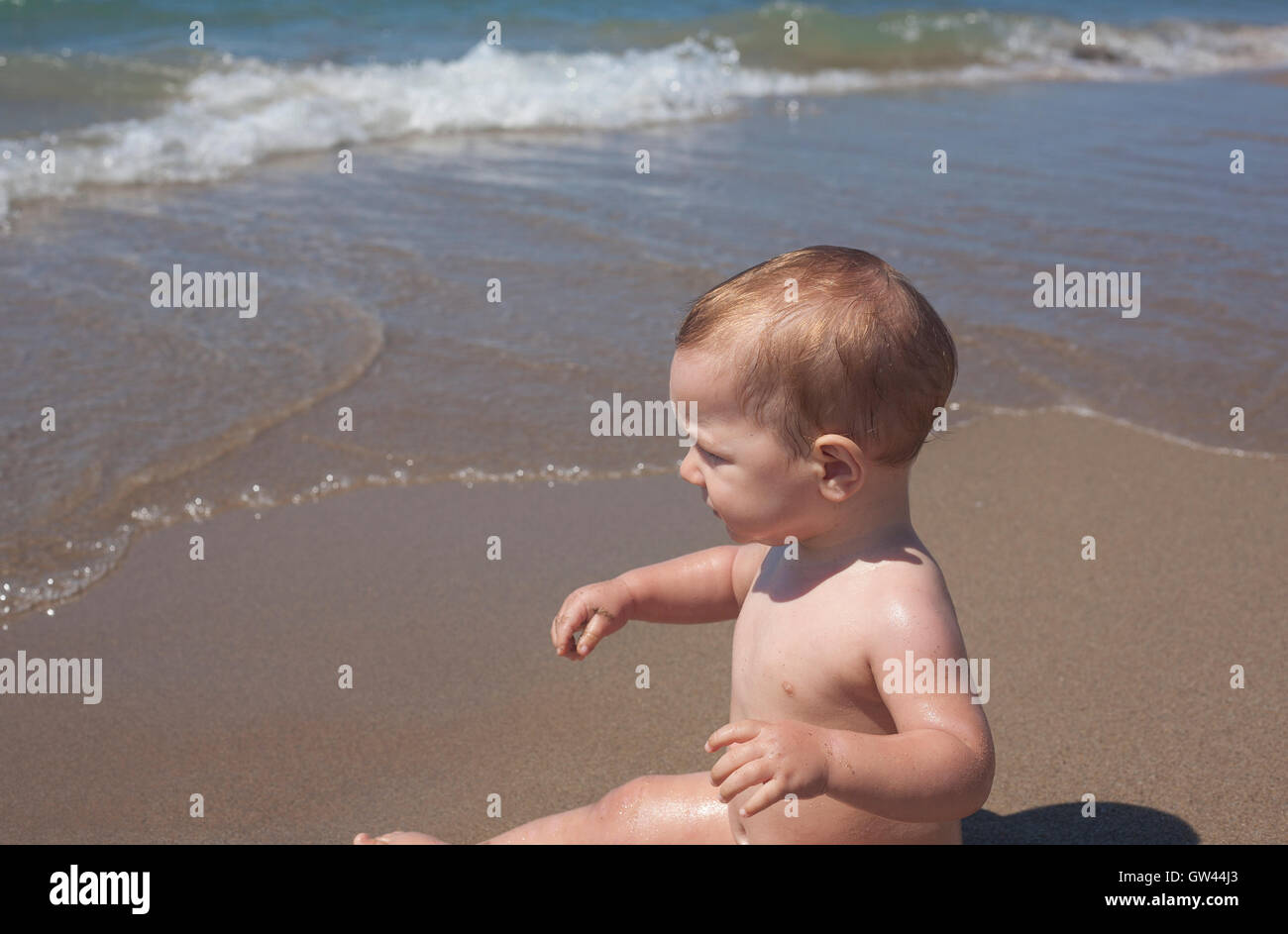 Happy Baby Boy sentado en la arena y observar el mar en la playa Foto de stock