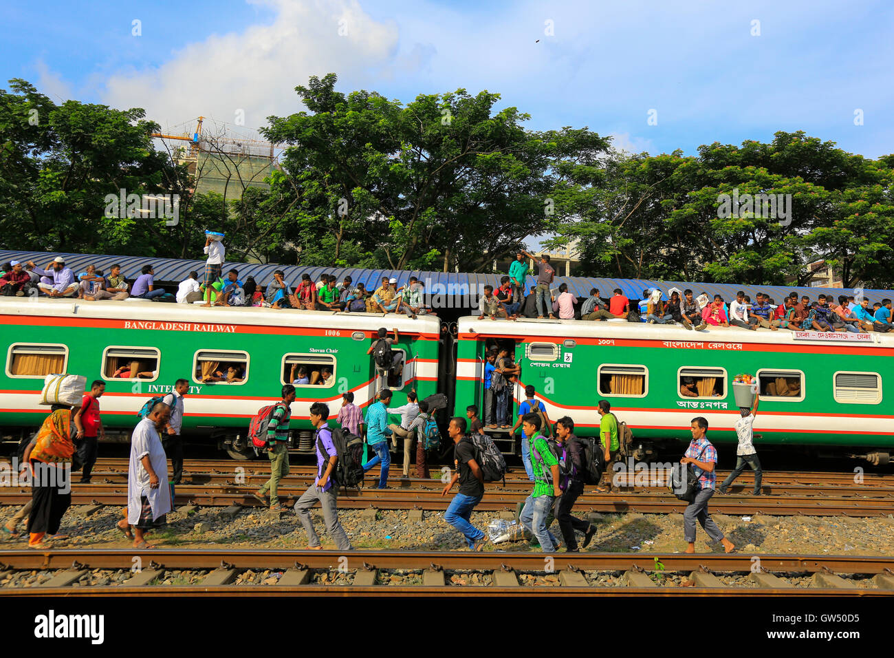 Las personas de bajos ingresos sobrecargar el techo de un tren en la estación de tren del aeropuerto de Dhaka mientras viajan, arriesgando sus vidas, a sus Foto de stock