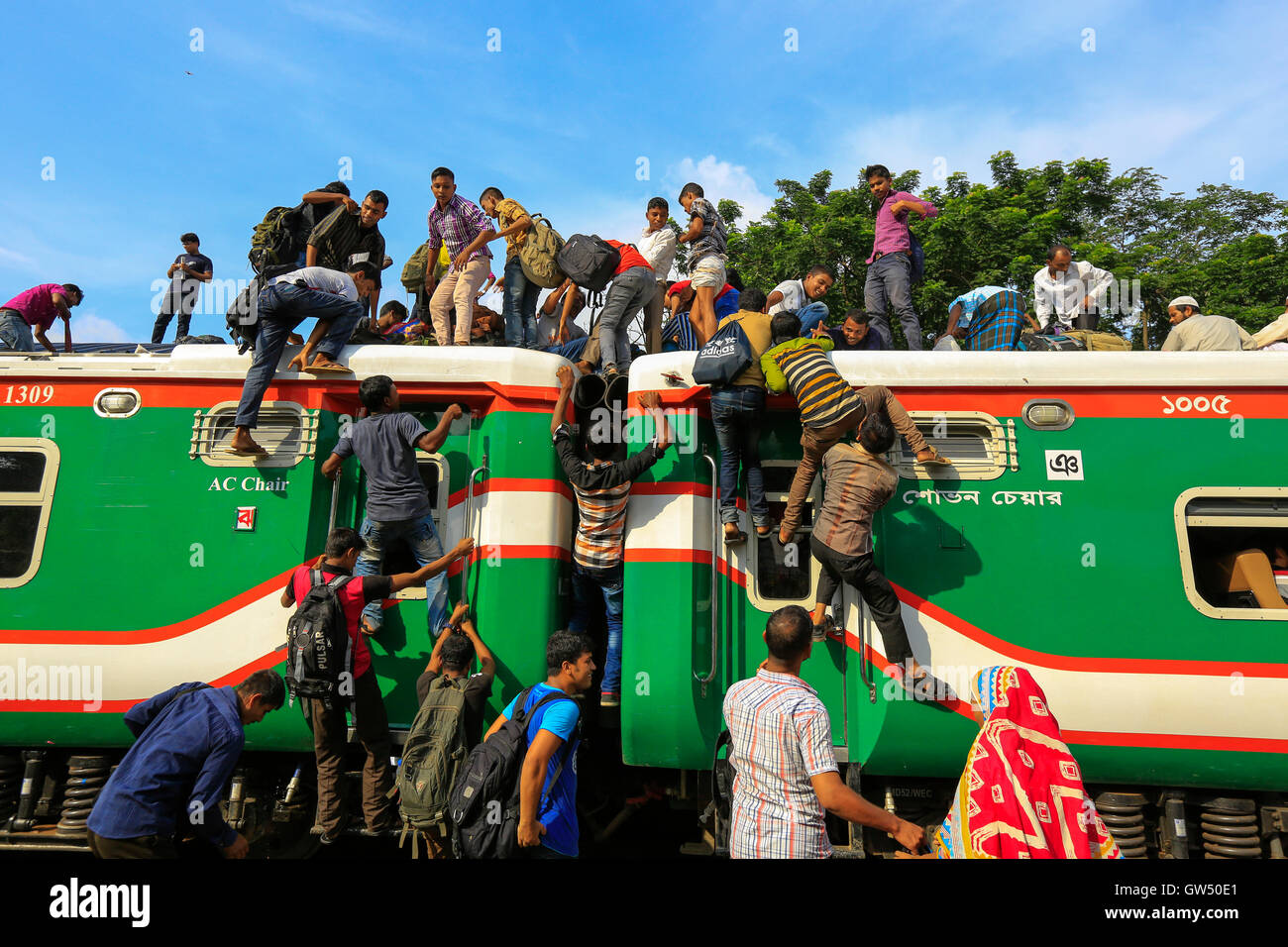 Las personas de bajos ingresos sobrecargar el techo de un tren en la estación de tren del aeropuerto de Dhaka mientras viajan, arriesgando sus vidas, a sus Foto de stock