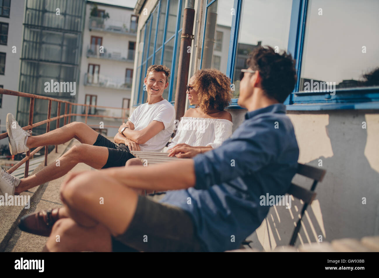 Tres jóvenes amigos en la cafetería al aire libre. Grupo multirracial de jóvenes relajarse al aire libre en la mesita de café. Foto de stock