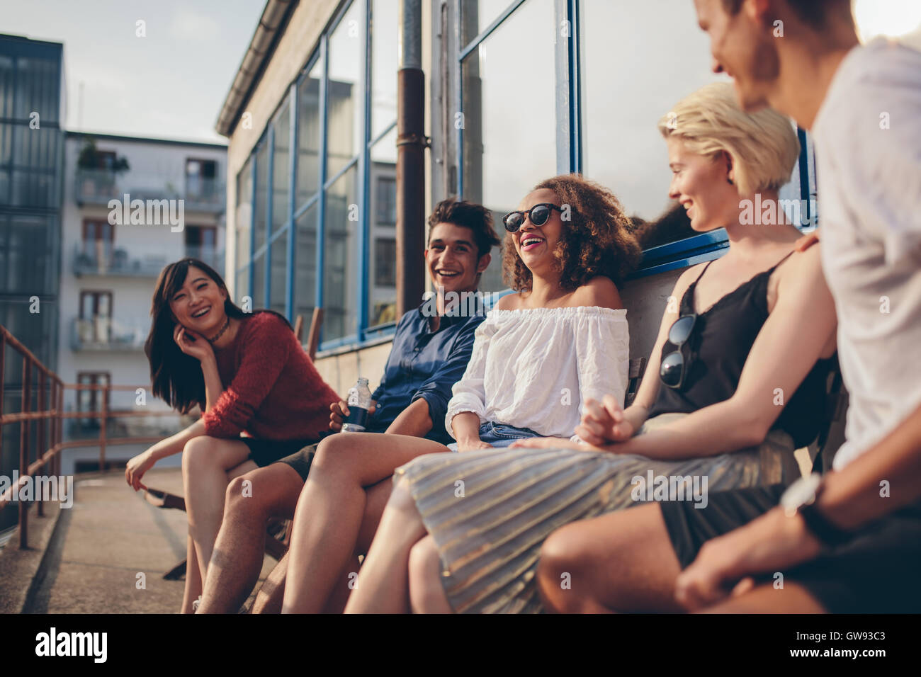 Grupo multirracial de amigos sentados en el balcón y sonriente. Los jóvenes relajarse al aire libre en la terraza. Foto de stock