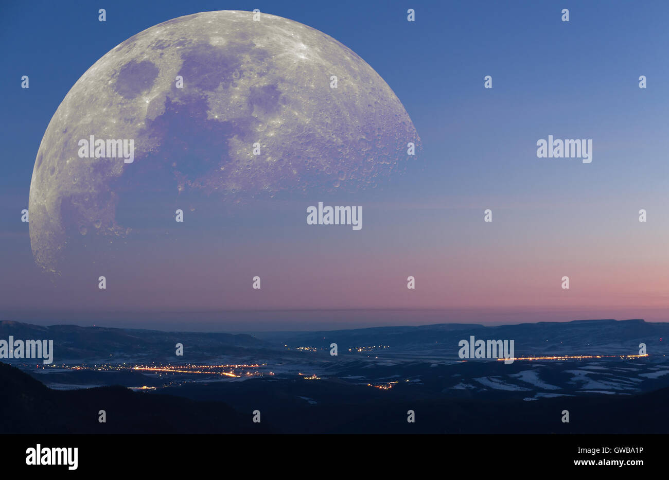 Fantástico paisaje: invierno temprano en la mañana vista desde las montañas hasta un valle con las ciudades de emitir luz con enormes derivados luna Foto de stock