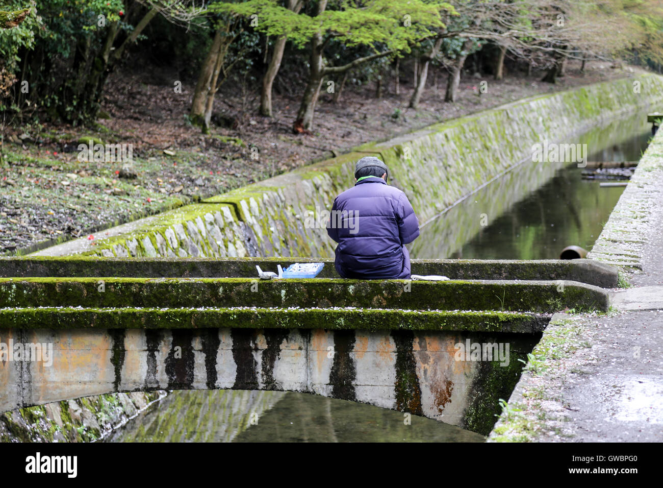 Fisherman preparando cebo sentado en un puente por encima de un canal Foto de stock
